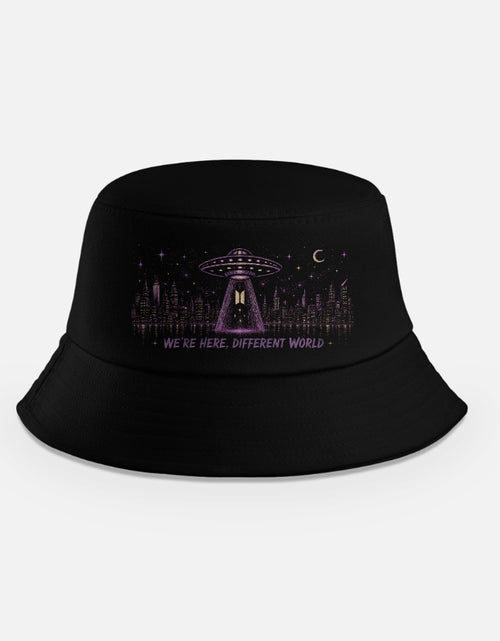 Black bucket hat with purple UFO beaming light over a city skyline at night with text we're here different world, BTS alien theory inspired design"